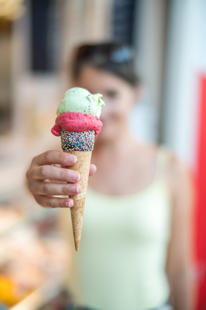 About Woman holding a vibrant ice cream cone topped with sprinkles, creating a refreshing summer treat.