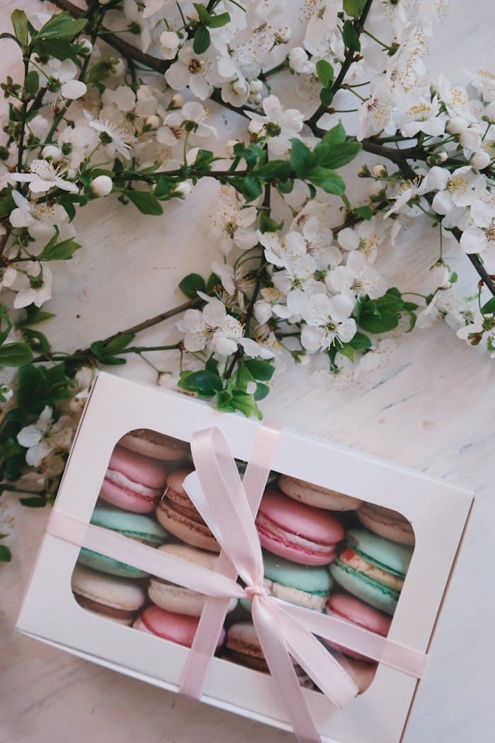 Home Charming box of assorted macarons wrapped in ribbon, placed with white cherry blossoms on a table.