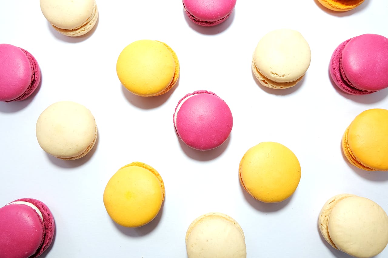Vibrant pink, yellow, and cream macarons arranged in a flatlay on a white background.